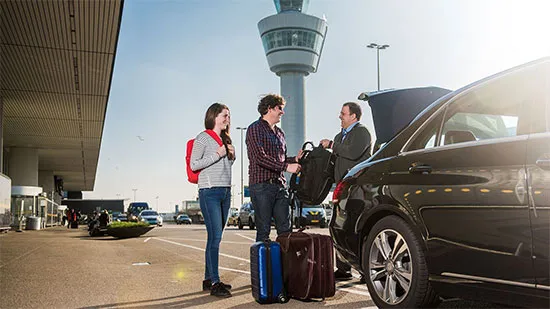 A male and a female student getting handed their luggage by the private taxi driver at the airport